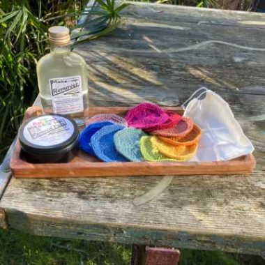Bottle of make up remover and colourfull hand knitted reusable make up removal pads with muslin bag to wash them in and tin box as packaging.
